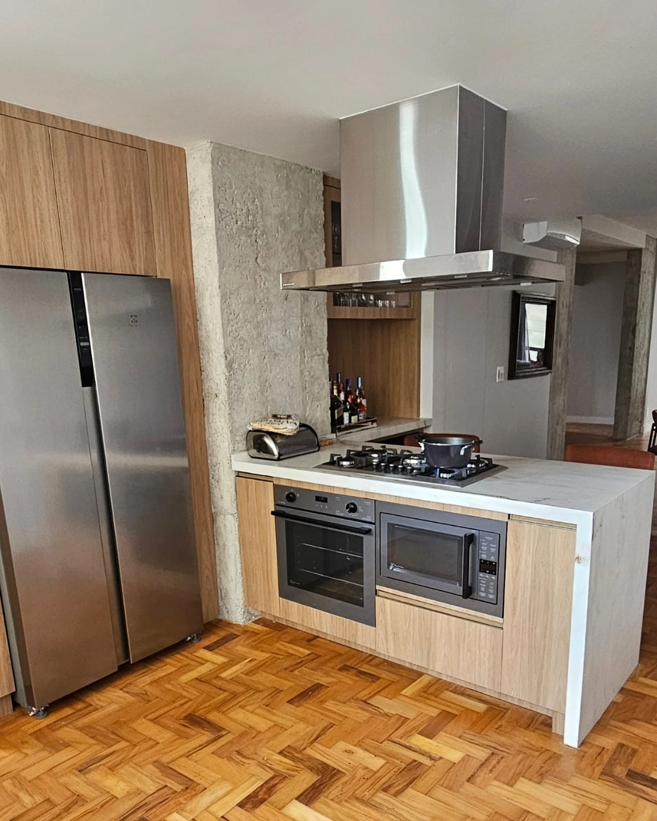 Coifa de ilha residencial em aço inox instalada sobre cooktop em cozinha integrada